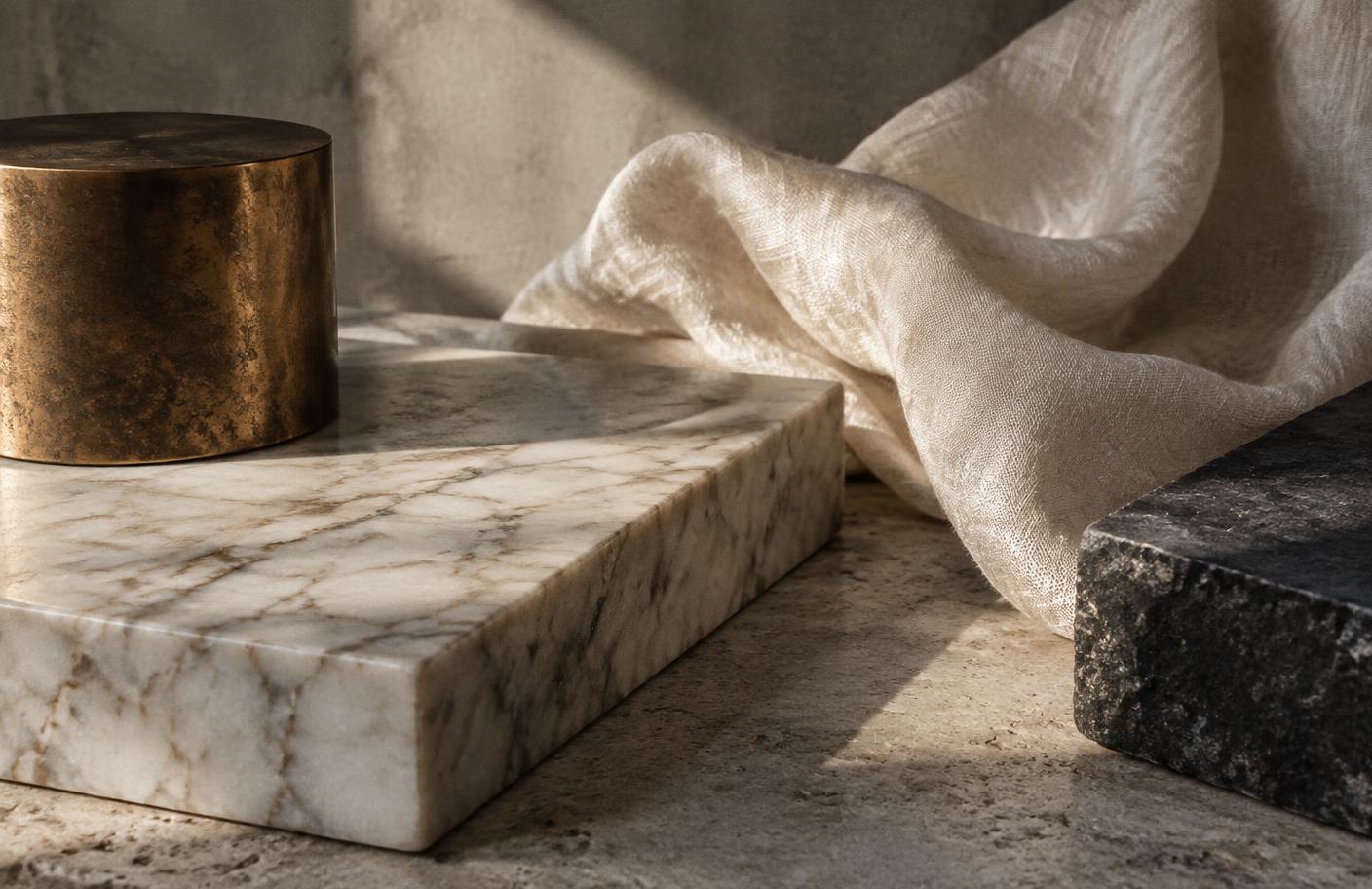 Honed marble, cast bronze, raw silk, and dark stone in natural light